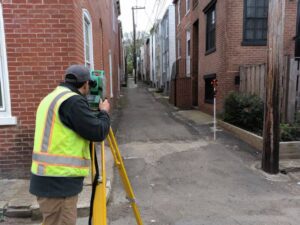 Boundary surveyor measuring a narrow Washington DC alley lot beside brick rowhouses
